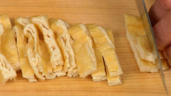 With a paper towel, remove the excess oil from the aburaage, thin deep-fried tofu. Cut it in half and slice it into 1cm (0.4") strips.