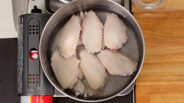 Next, let’s make the delicious chicken broth. In a pot, arrange the parboiled chicken wings. Pour in the water. Add the sake.