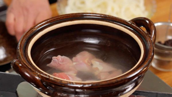 Let's make Miso Nikomi Udon. Heat the dashi stock in an earthen pot also known as donabe, and place the chicken into it.