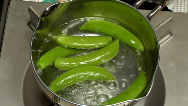 Remove the firm stringy fibers from the snap peas. Add a pinch of salt to boiling water. Immerse the snap peas.