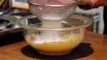 Placez une passoire sur le bol, et ajoutez la farine à gâteau et la fécule de maïs. Tamisez les poudres, et mélangez jusqu'à ce que ça soit homogène. 
