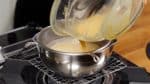 Now, place a mesh strainer over the pot of milk, and pour in the egg mixture. This process will remove any white egg chalazas and pockets of dry flour, making the cream very smooth.