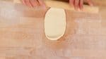 Then, using a rolling pin, roll the dough back and forth, shaping it into a flat oval.