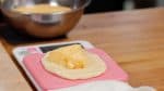 With a scraper, gently remove the dough, and place it onto a kitchen scale with the clean side facing down. Measure out 35g (1.3 oz) of the pastry cream on the dough, and place it onto the kneading board.