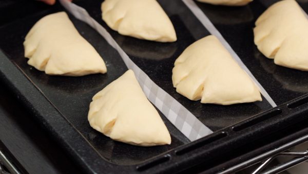Remove the plastic wrap. To keep the dough from sticking, we are placing strips of parchment paper in between. For the second fermentation, mist the dough with water if your oven doesn't have a steam function.