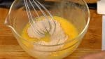 Als nächstes schlag die Eier in einer Schüssel mit einem Schneebesen auf. Füge den Zucker hinzu und rühr, damit der Zucker sich auflöst.
