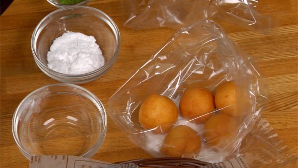 Let’s coat the donuts with sugar. Put the powdered sugar into a food storage bag. Put half of the donuts into the bag. Shake to coat with the sugar.