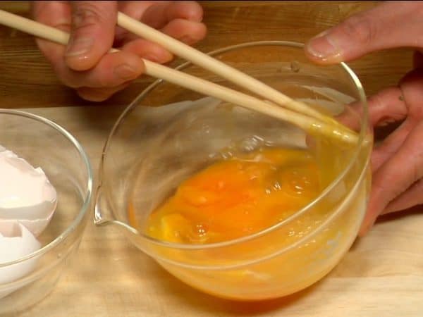 Đập 2 quả trứng vào bát. Làm vỡ lòng trắng trứng bằng đũa để giúp nó đều ra và rau đó đánh nhẹ trứng. Cẩn thận không đánh trứng quá tay nếu không sẽ mất đi kết cấu mướt.