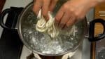 Let's cook the udon noodles. Boil a generous amount of water in a large pot. Lightly shake off the corn starch and submerge half of the udon noodles in the boiling water.