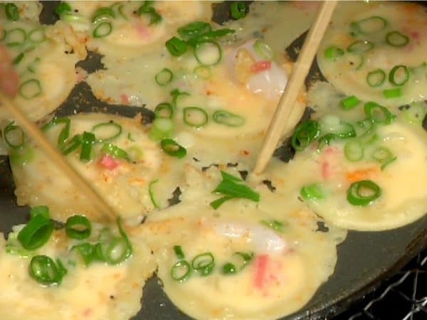 When the batter around the holes cooks, separate each takoyaki from the pan with bamboo skewers.