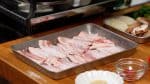 では回鍋肉を作ります。豚肉をトレイに並べ、片栗粉を振りかけます。片栗粉でコーティングすることにより、肉は固くなりにくく調味料がよく絡みます。豚肉を返し裏にも片栗粉を振りかけます。