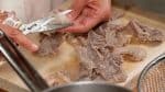 Placez le gyusuji sur une planche à découper et retirez l'excès d'eau avec un papier absorbant. Avec des ciseaux de cuisine, découpez les tendons en grandes bouchées et retirez la graisse.