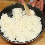 Den frisch gekochten Reis in ein flaches Gefäss geben und gleichmässig verteilen. Abkühlen lassen und die überschüssige Flüssigkeit verdampfen lassen.