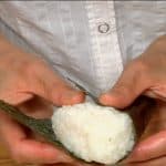 Enrolla el onigiri con el alga triangular. Deja la parte brillante del alga hacia fuera. 