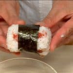 Die Hände mit Salzwasser befeuchten und die Reismischung zu einem Zylinder formen. Mit dem kurzen Nori-Streifen umwickeln.