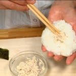 Cho cơm nắm onigiri sốt mayonnaise cá ngừ, để sốt Mayonnaise cá ngừ lên cơm và nặn cơm nắm onigiri thành hình tròn phẳng.