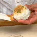 Für das Negi-Miso-Onigiri die Hände mit Salzwasser befeuchten und eine Portion Reis zu einem etwas festeren Dreieck formen. Mit einem Spachtel beide Seiten mit Negi-Miso-Paste bestreichen.
