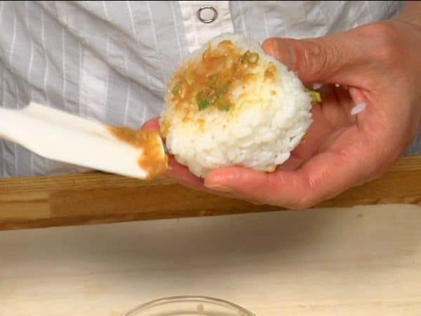 Selanjutnya, mari kita membuat Onigiri Negi Miso. Basahi tangan Anda dengan air garam dan bentuk nasi menjadi segitiga. Dengan spatula, tutupi kedua sisi onigiri dengan pasta negi miso.
