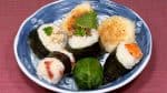 Servez les onigiri sur une assiette et garnissez-la avec les feuilles de shiso, le persil, les feuilles de kinome et les graines de sésame blanc.