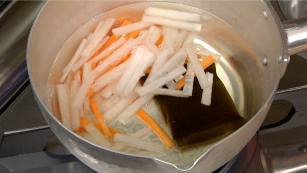 Let’s make the tsumire-jiru. Put the daikon radish and carrot into the pot of the kombu dashi stock, turn on the burner and cover with a lid.