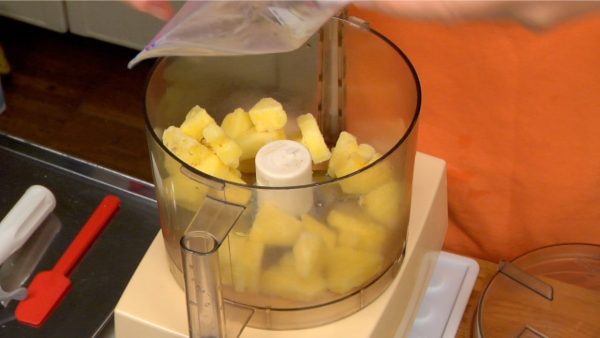 Let’s make the ice cream. Place the frozen pineapple into a food processor.