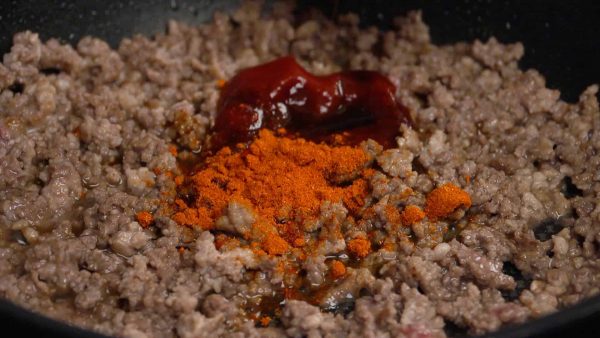 Pour éviter que ça brûle, baissez le feu avant d'ajouter les assaisonnements. Maintenant, ajoutez le ketchup, la sauce worcestershire japonaise et le mélange de chili en poudre. 