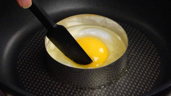 Then, place the egg into the egg ring. With a spatula, keep the yolk in the center until the white begins to firm up. Sprinkle on the salt and the pepper.