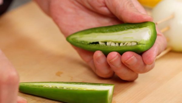 And now, let’s cut the vegetables. Remove the stem end of the bell pepper. And cut it in half lengthwise. Trim off the stem end and remove the seeds.