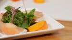 Sắp xếp món khai vị xung quanh rau củ non dùng cho rau trộn (salad) trên đĩa. Trang trí bằng các múi hồng tối đa.
