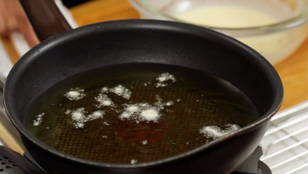 Et maintenant, avec des baguettes de cuisine, mélangez l'huile de friture pour uniformiser la température. Versez quelques gouttes de pâte dans l'huile pour vérifier si la température atteint 170°C (338°F). Quand la pâte plonge au fond et remonte rapidement à la surface, l'huile devrait être à la température appropriée. 
