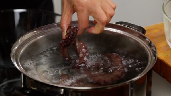 Now, let's cook the octopus. Boil a generous amount of water in a large pot. Submerge the octopus into the boiling water and cook for about 5 minutes.