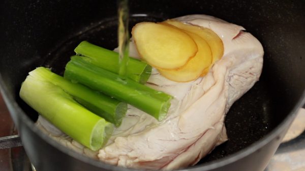 Next, place the chicken into another pot. Add the green part of a long green onion and ginger root slices. Add the sake and salt.