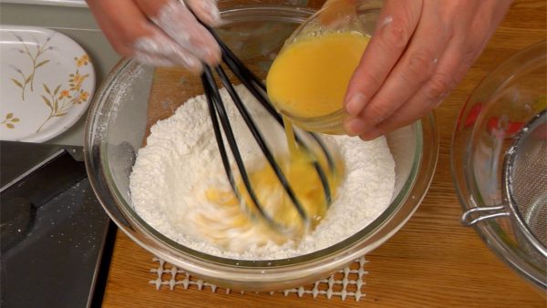 Pour the beaten egg into the center of the flour while mixing.