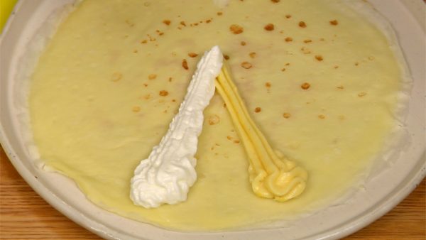 Next, let’s make the banana crepe. Place the crepe onto the plate with the first baked side facing down. Squeeze out the custard and whipped cream, making a "V" shape.