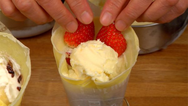 Let’s place the ice cream into the crepes and decorate them with the toppings. Place a scoop of the vanilla ice cream into the strawberry crepe and garnish with the strawberry slices.