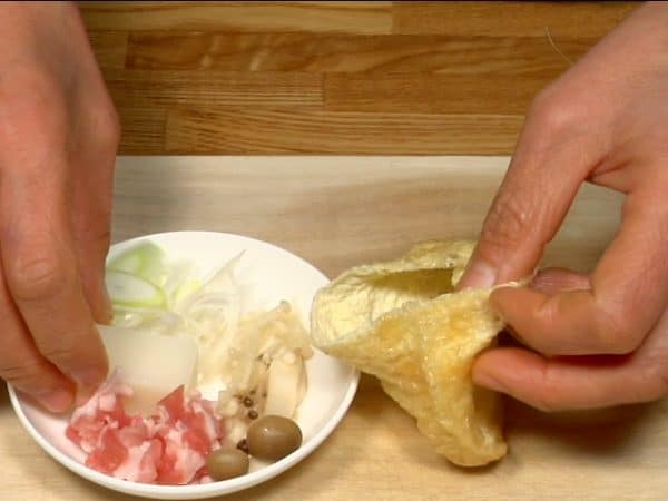 Let's make takarabukuro, which means treasure bag in Japanese! Open the aburaage, a thin deep fried tofu pouch and place the mochi, sliced pork, naganegi, and mushrooms into it.