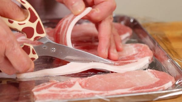 Tiếp theo, bằng kéo nhà bếp, cắt bỏ mỡ thừa từ các lát thịt thăn lợn (heo).