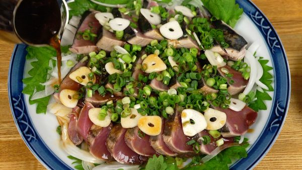 Distribute the garlic slices onto the katsuo and sprinkle on the chopped spring onion leaves. Pour the sauce over it.