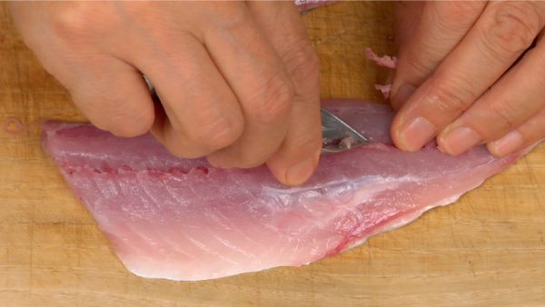 Next, remove the small bones from the center of the fillets. Pinch the small bone with kitchen tweezers and pull it out toward the head.
