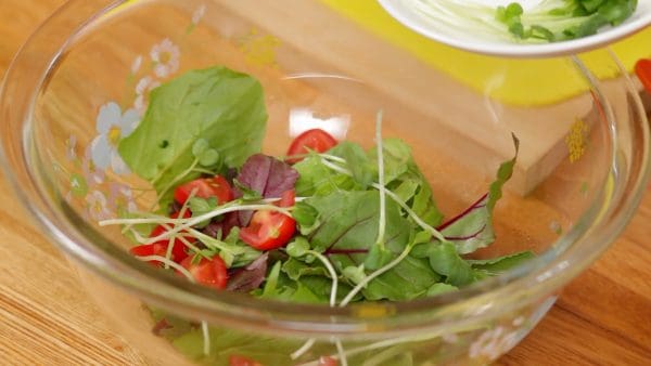 In a bowl, combine the baby salad greens, quartered cherry tomatoes, kaiware radish sprouts and sliced button mushrooms.