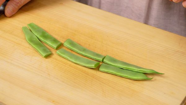 Next, remove the stem end of the string bean pods. Then, cut the bean pods into 3 equal pieces.