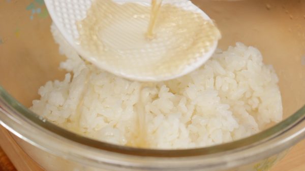 Now, place the fresh steamed rice into a bowl. Gradually pour the sushi vinegar over the rice paddle to distribute it evenly.