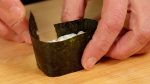 Enfin, revoyons l'opération d'enveloppement une nouvelle fois. A l'aide d'un grain de riz, entourez le riz à sushi avec le nori.