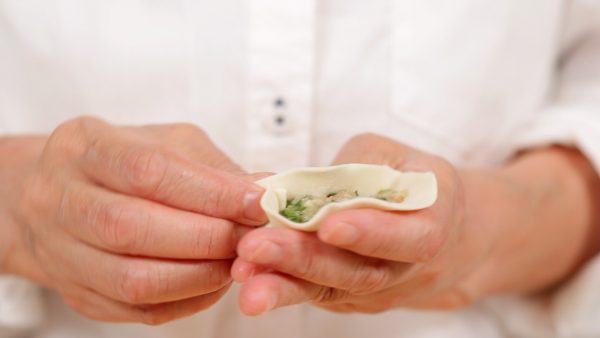Fold the wrapper in half and press the edges together while making small pleats on one side to give the gyoza its signature look.