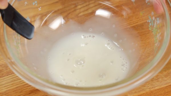 Primeiro, vamos fazer a massa. Adicione o leite quente ao mel em uma vasilha. Misture bem com uma espátula.