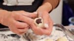 Nhấn anko và xoay bánh manju từng chút một trong khi đưa bột nhồi lên trung tâm bằng tay còn lại.