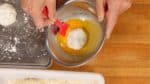 Dann entfernst Du vorsichtig überschüssiges Mehl von der Füllung und tauchst diese in das verquirlte Ei.