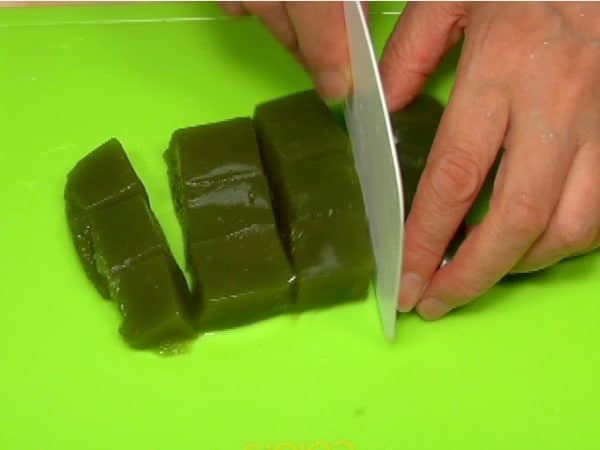 Dampen a pastry scraper to keep it from sticking, and cut the matcha kuzumochi into cubes.