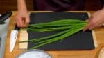 Faisons cuire les oignons verts wakegi. Pincez les pointes des feuilles de wakegi afin de les empêcher d'éclater dans l'eau bouillante.
