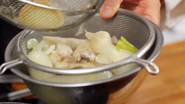 Remove the chicken wings and aromatic vegetables, and place them onto a strainer over a bowl.